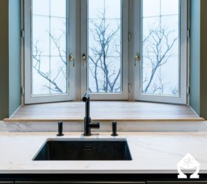 Évier noir associé à un plan de travail couleur marbre face à une fenêtre bow-window.