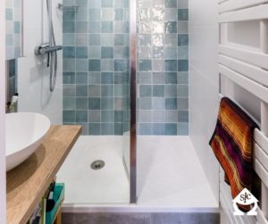 Douche avec des carreaux de différentes teintes de bleu ainsi qu'un receveur de douche re-coupable et surélevé.